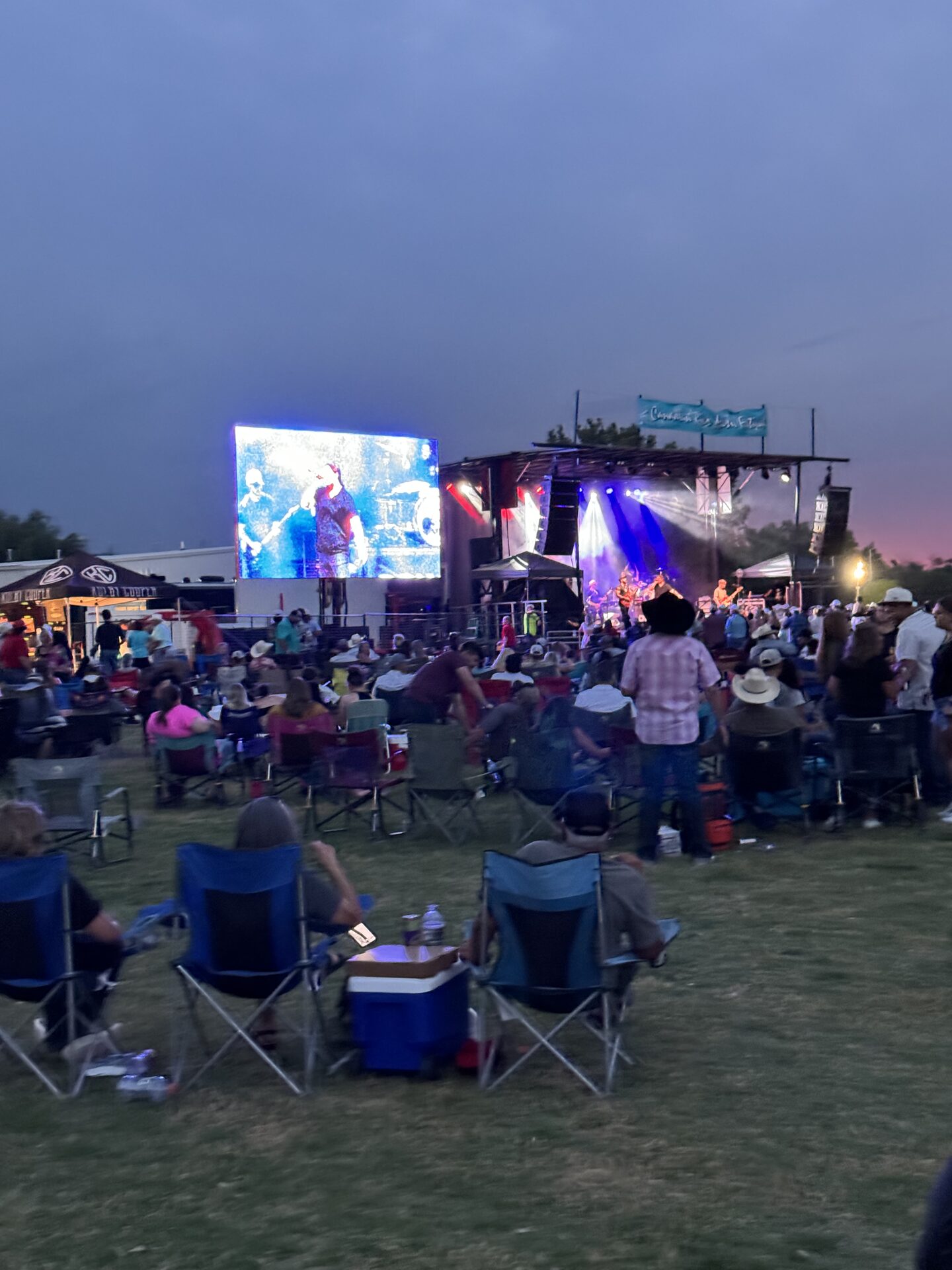 Festival goers in camp chairs at dusk watching the stage
